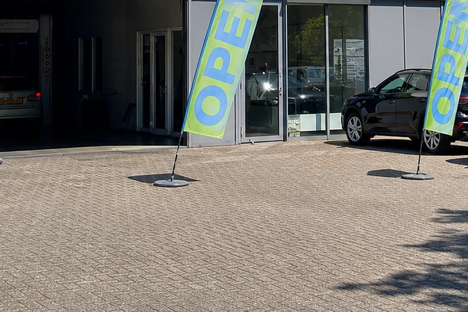 Ingang van een carwash met openstaande wasstraat en wachtende auto’s op het voorterrein